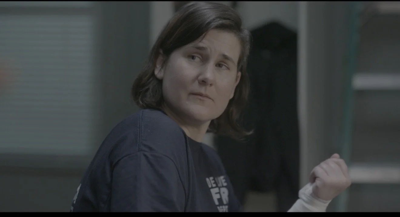A woman with short brown hair in a navy shirt looks over her shoulder with a concerned expression.