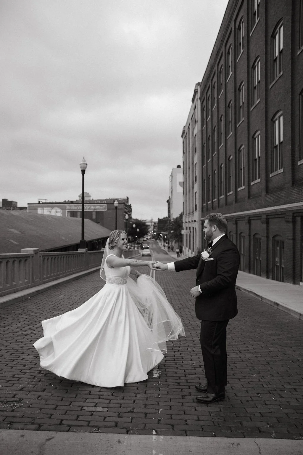 A bride and groom holding hands at Jackson Terminal and dancing on a city street, with the bride in a wedding dress and veil, and the groom in a suit with a flower boutonniere, black and white photo.