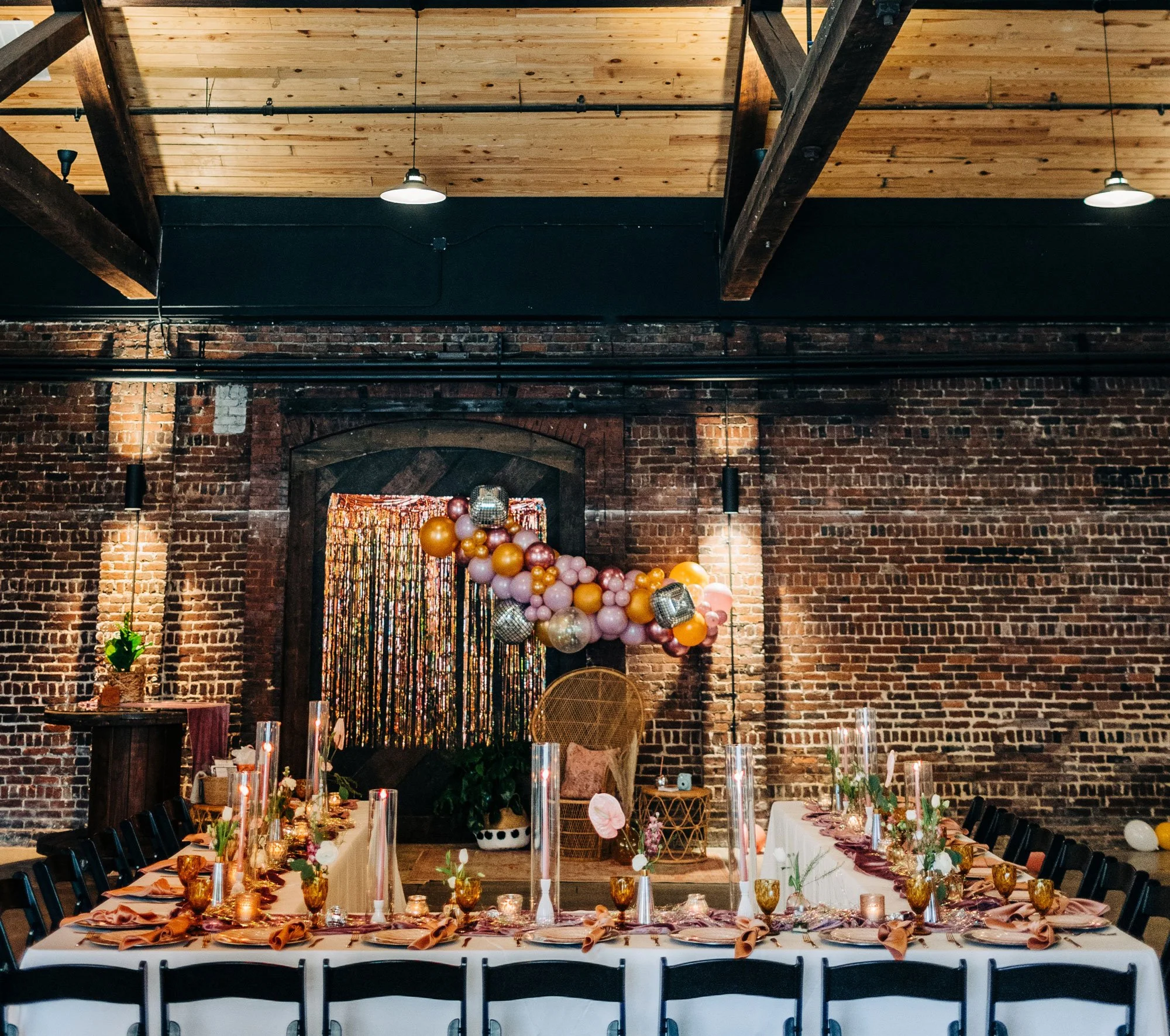 Decorated banquet table in Downtown Knoxville wedding venue set for a celebration with balloons, candles, and floral arrangements, against exposed brick walls and a wooden ceiling.