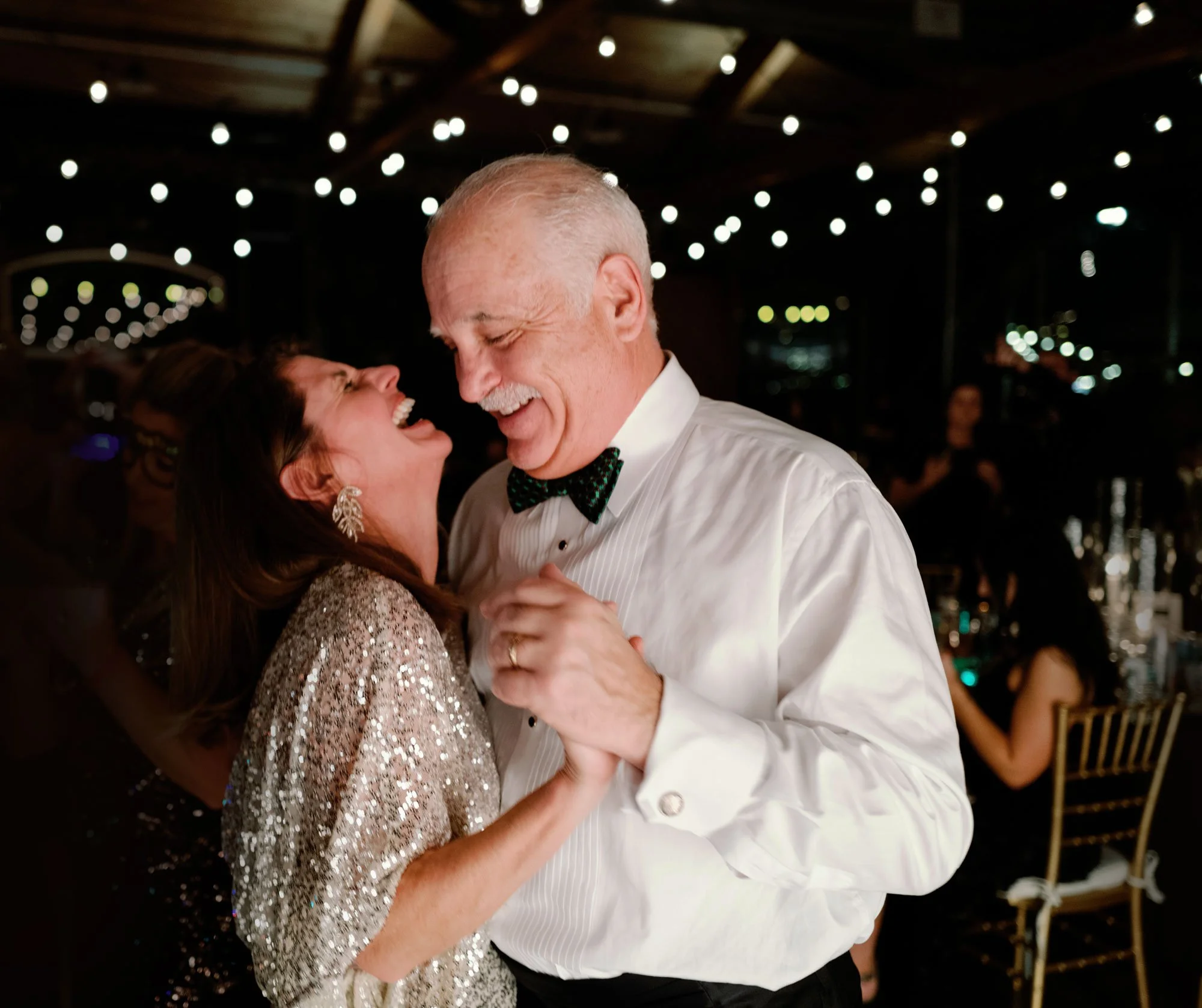 A happy couple dancing in Knoxville at a celebration, with string lights above them in a dark setting.