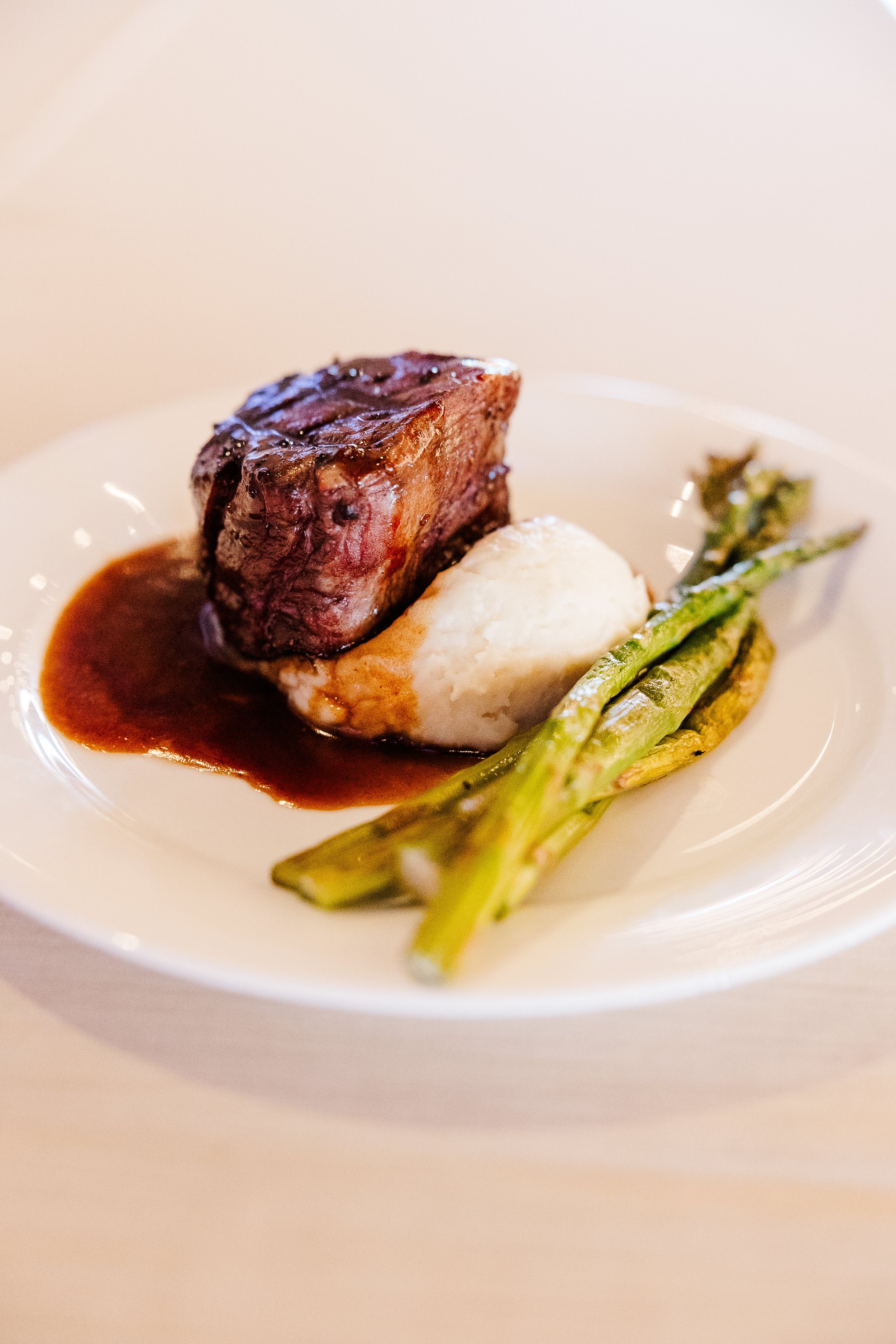 A catered plate in Knoxville with a piece of cooked beef steak, mashed potatoes, and grilled asparagus with a brown sauce.