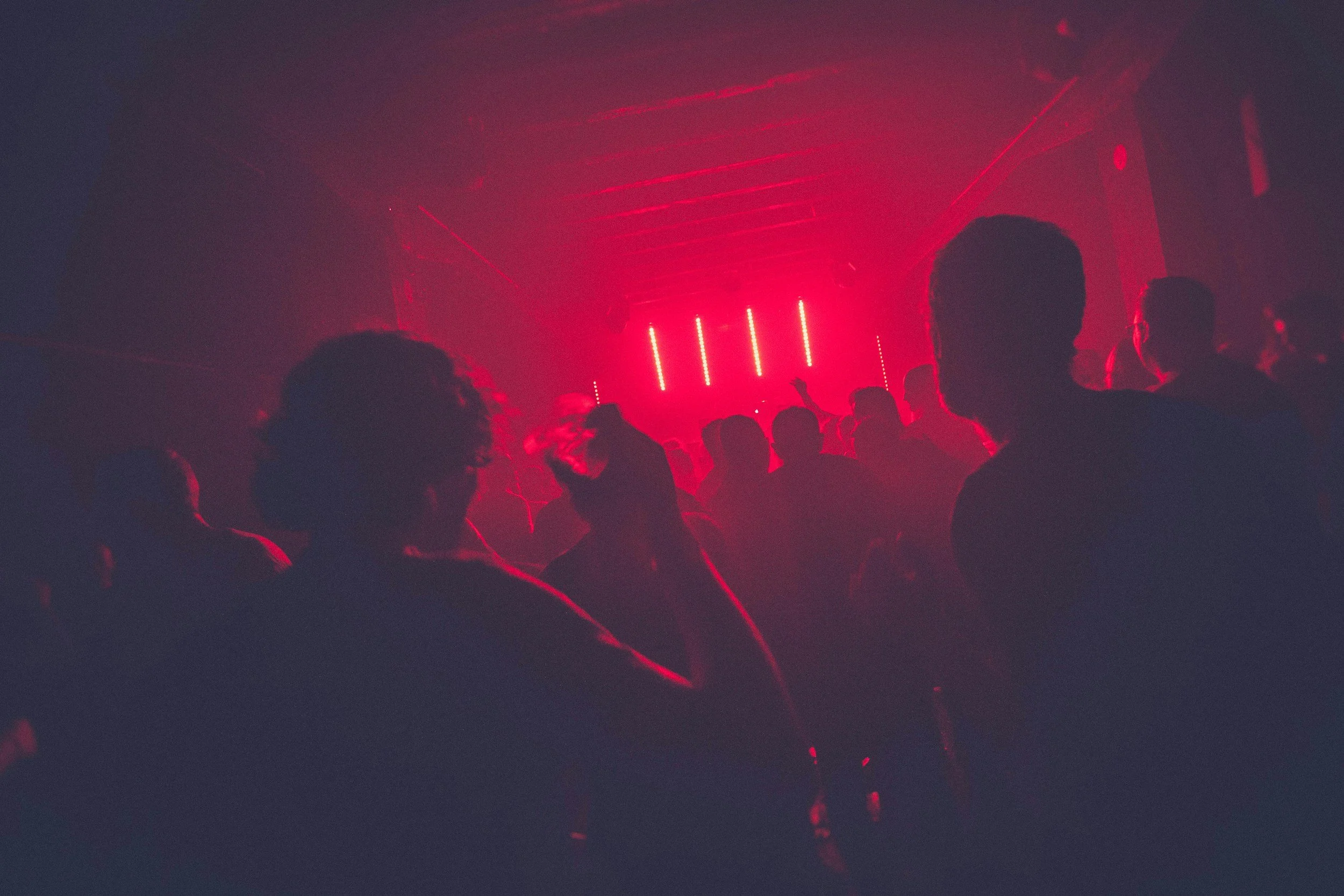 A dark indoor dance party with people dancing and red laser lights creating a vibrant atmosphere.