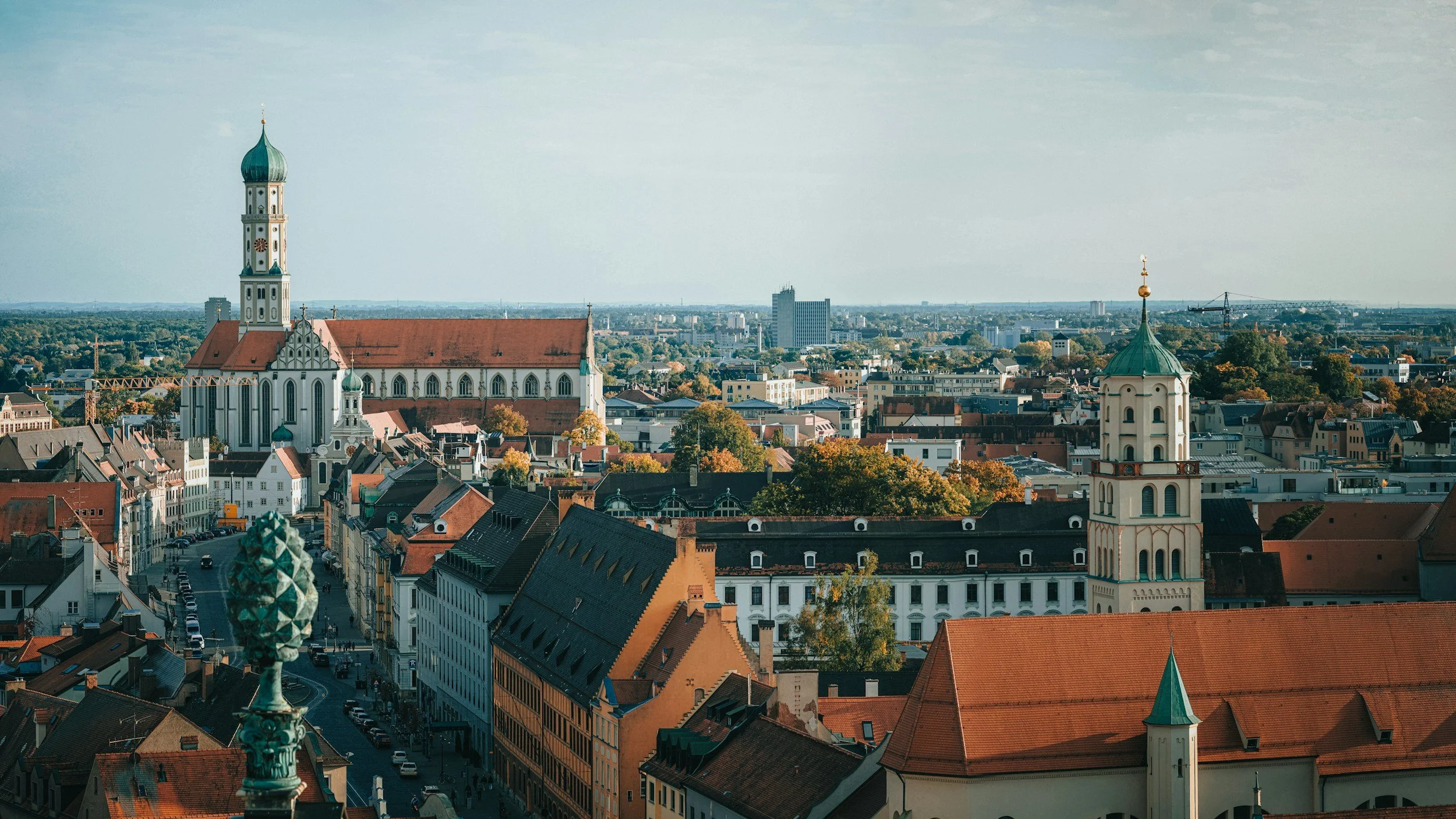 A city skyline featuring historic and modern buildings, with a church with a tall spire in the foreground, and trees with autumn foliage.
