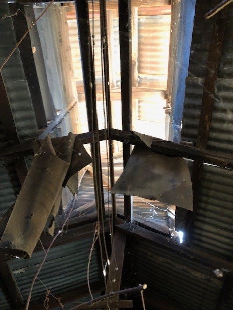 Interior view of a Chinese skywell in disrepair, torn and bent metal roofing and framing, exposing outside sunlight.