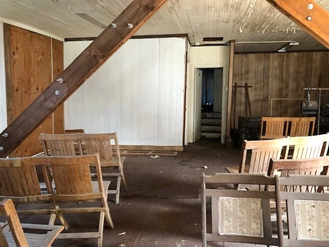Empty theaterbwith wooden chairs, a staircase, and wood-paneled walls, appears abandoned or unused.