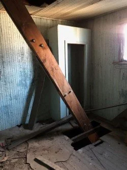 Dilapidated room on the theater stage with a wooden beam brace stabilizing the building, white wardrobe near a window.