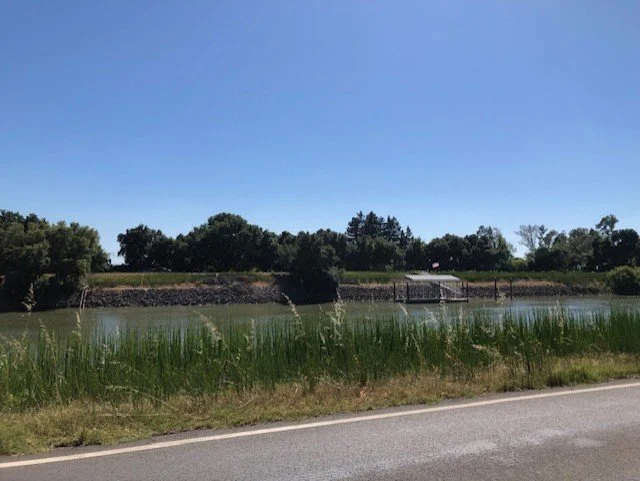 The Sacramento River with the River Road under a clear blue sky.