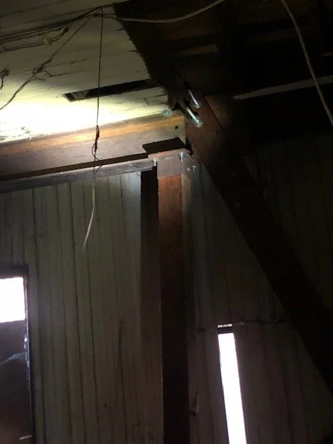 Interior of the ground floor level showing a detached  I-beam, natural light entering through holes in the exterior siding.