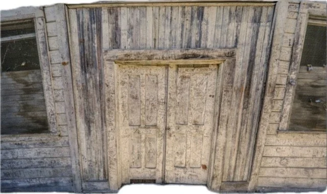 Old weathered wooden door with faded paint and visible wood grain, set within a similarly aged wooden wall.