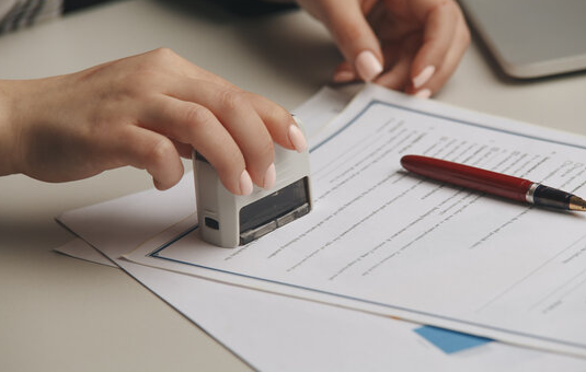 Person stamping a document with a rubber stamp on a desk.