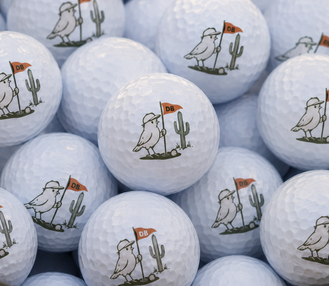 Close-up of several white golf balls featuring a cartoon seagull wearing a hat, standing next to a cactus, holding a red flag with 'DB' on it.