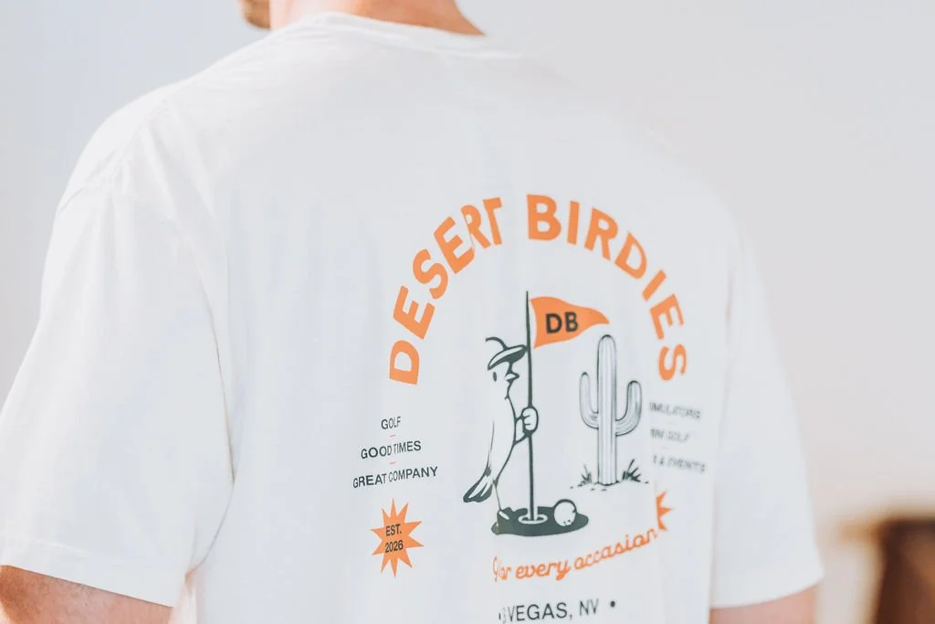 Close-up of a white T-shirt with a desert theme graphic and text, worn by a person, showing part of their back and shoulder.
