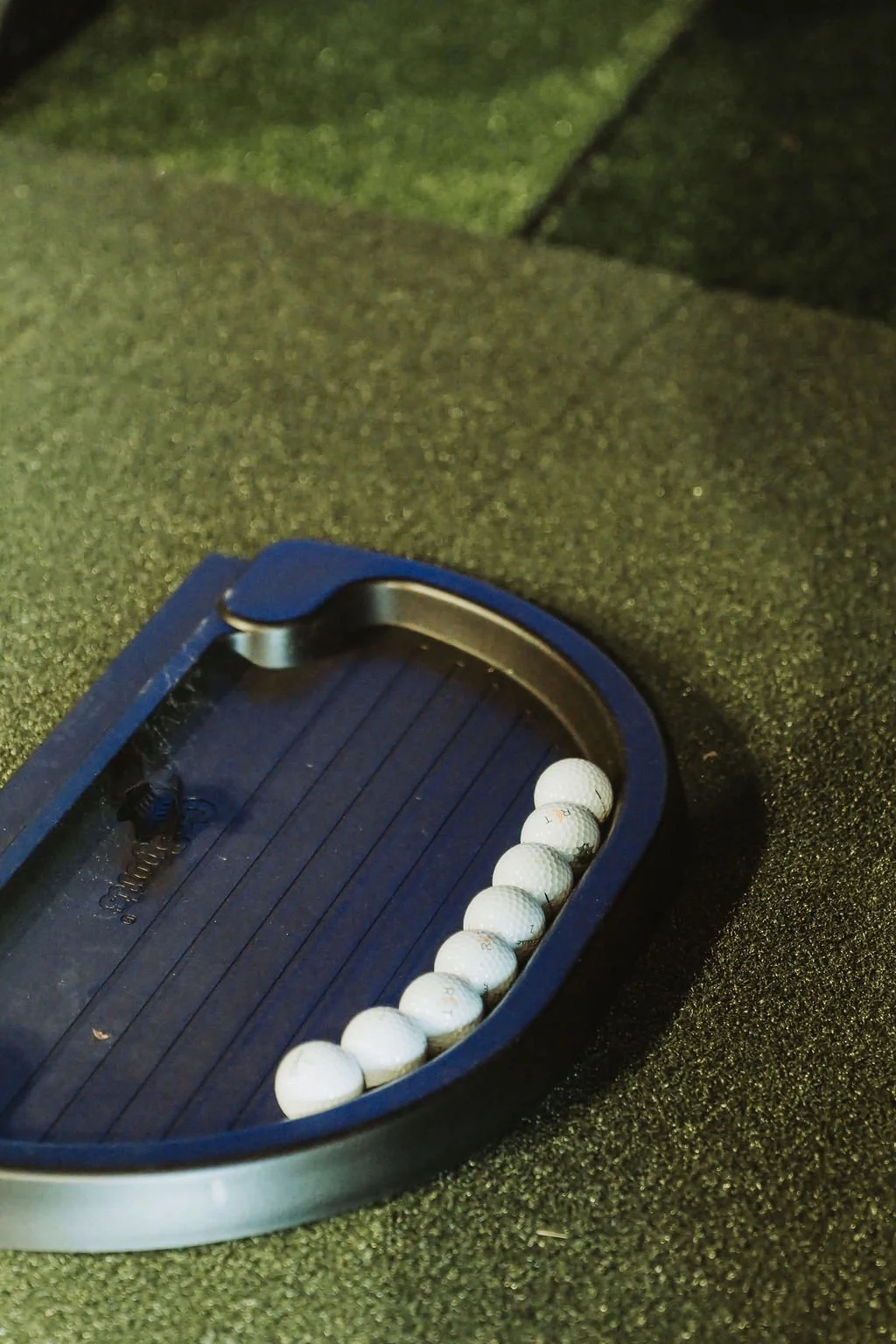 A golf putting practice device with a row of white golf balls inside a blue plastic case on a green textured surface.