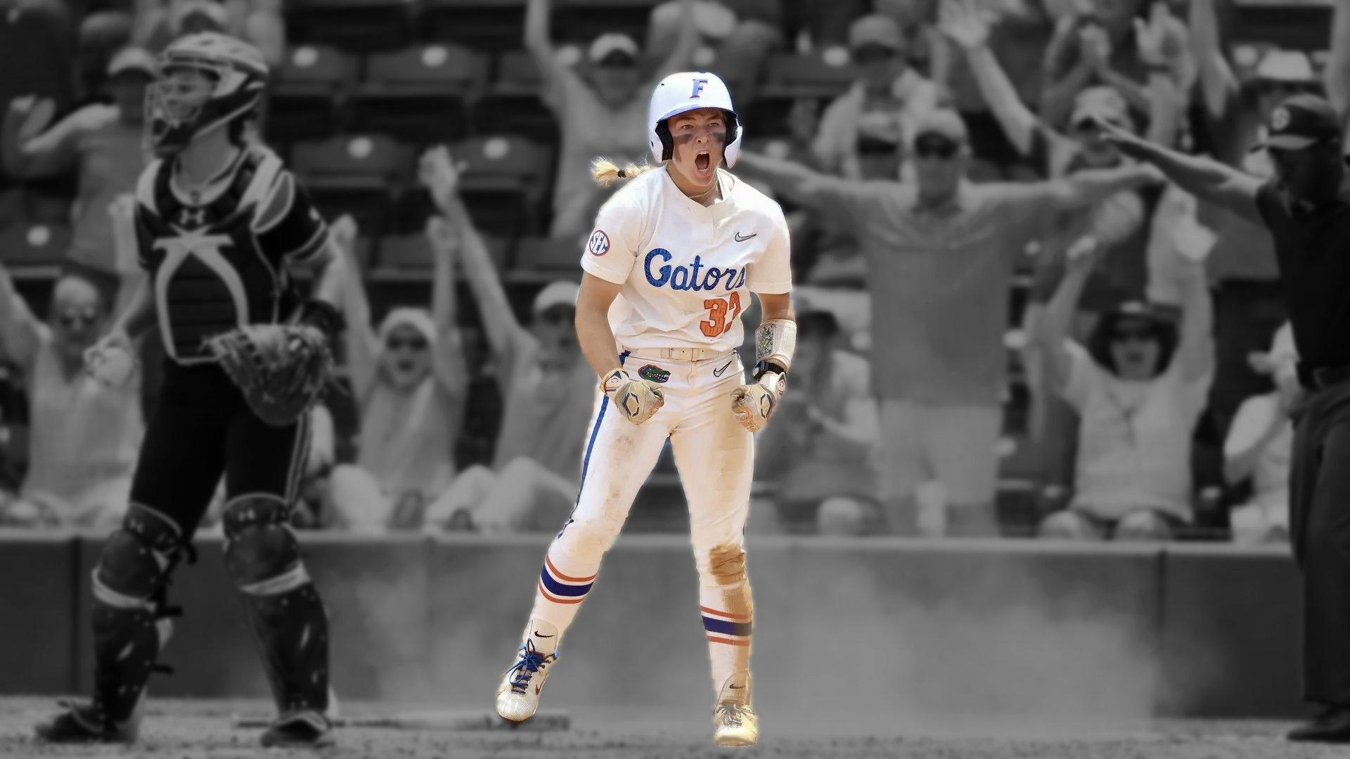 A female softball player in a Gators uniform celebrates with an intense expression on her face during a game, with fans cheering in the background.