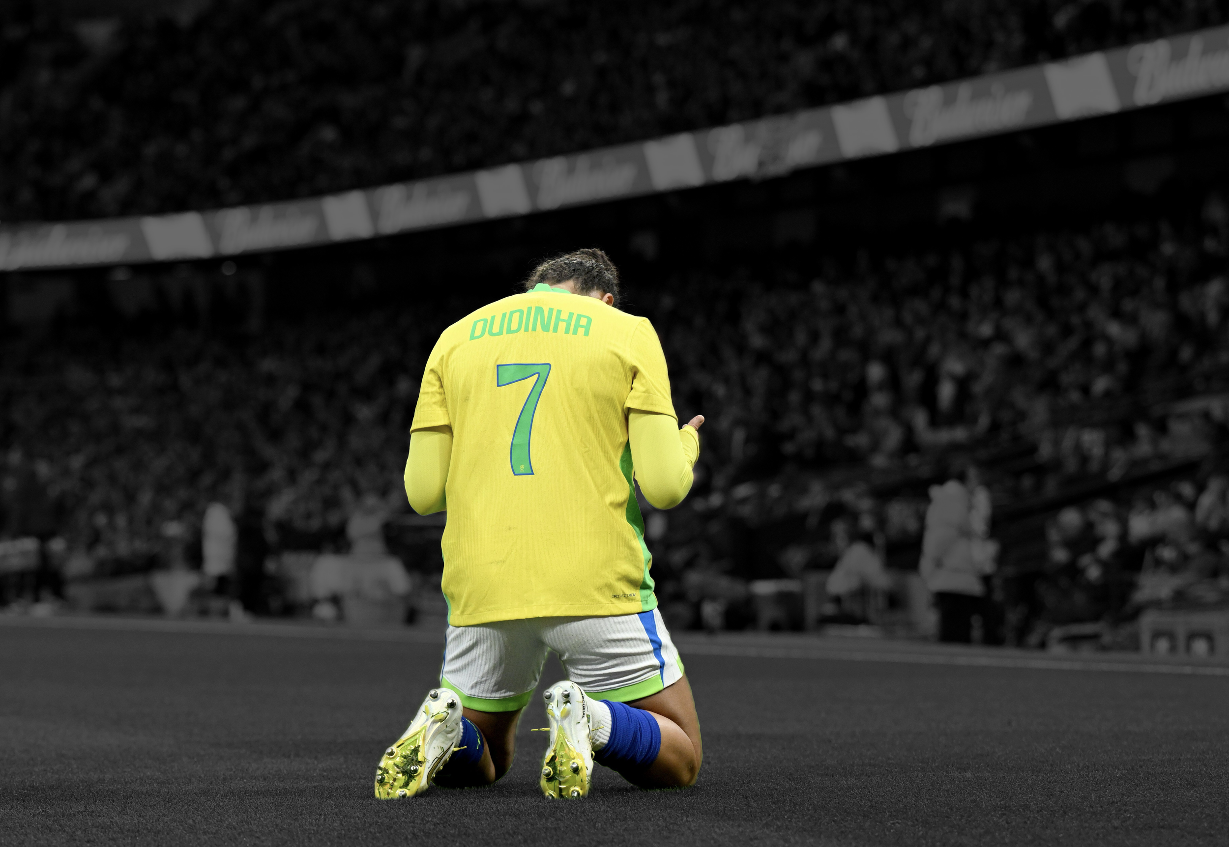A soccer player from Brazil kneels on the field with his head bowed, a teammate embraces him from behind, inside a stadium with a dark background.