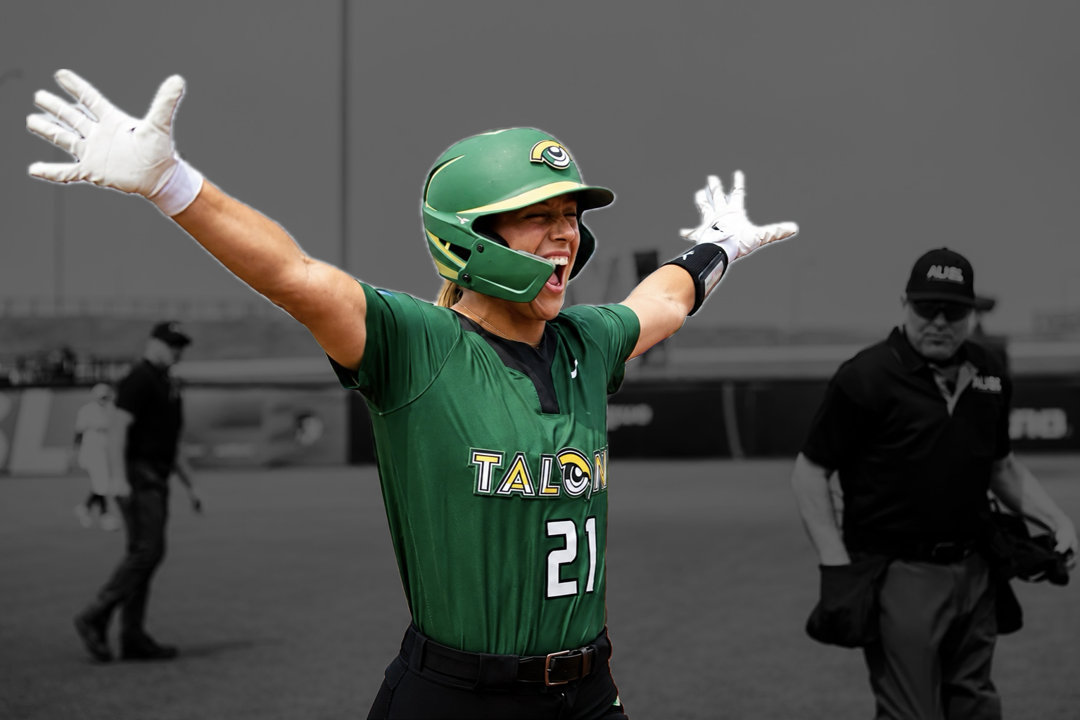 A woman in a green football jersey and helmet, with arms raised, celebrating on the field.