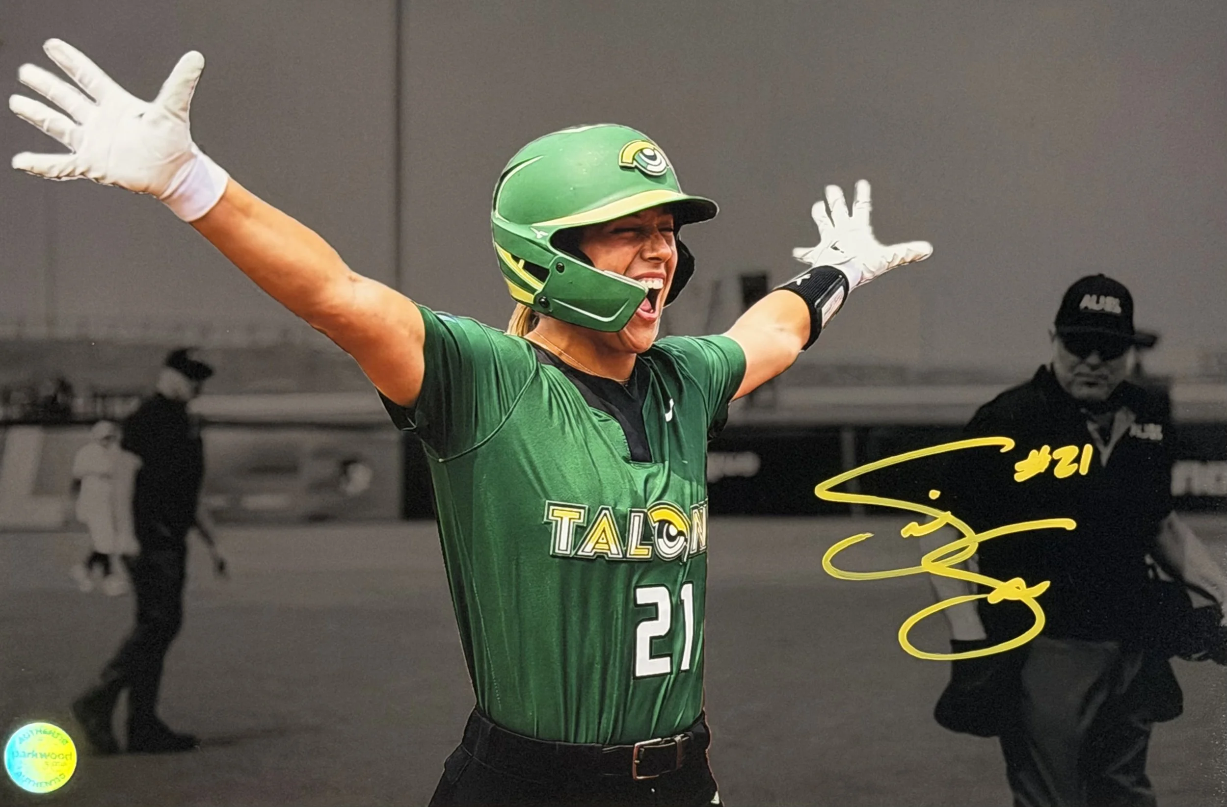 A woman in a green football jersey and helmet, with arms raised, celebrating on the field.
