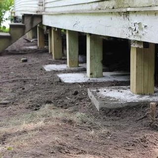 Close-up of the underside of a wooden deck with support beams and concrete footings in a yard.