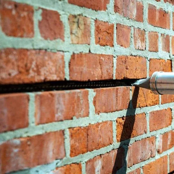 Close-up of a screwdriver screwing into a brick wall to secure a cable or wire.