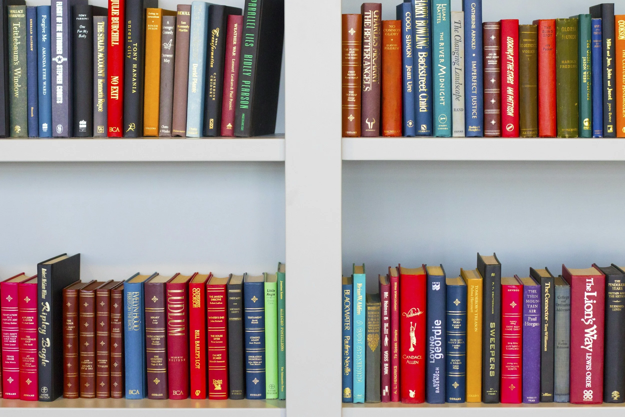 Two white bookshelves filled with colorful books organized vertically, with a clear blue wall in the background.