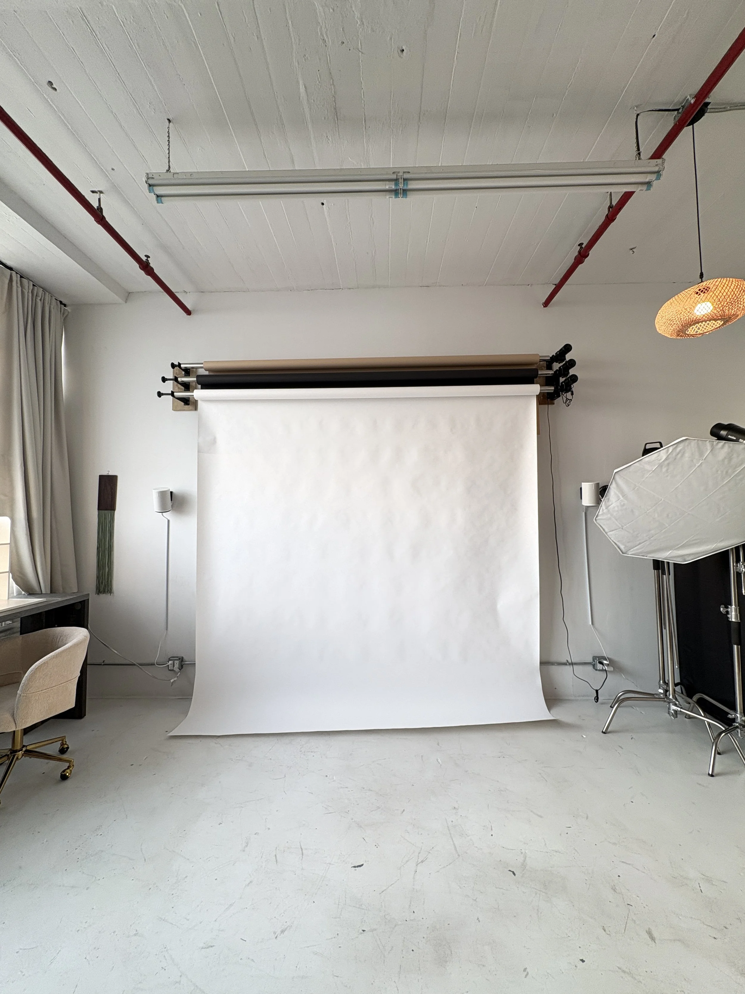 Photography studio backdrop setup with white seamless paper and boom arm, photography lights, and studio accessories in a photostudio
