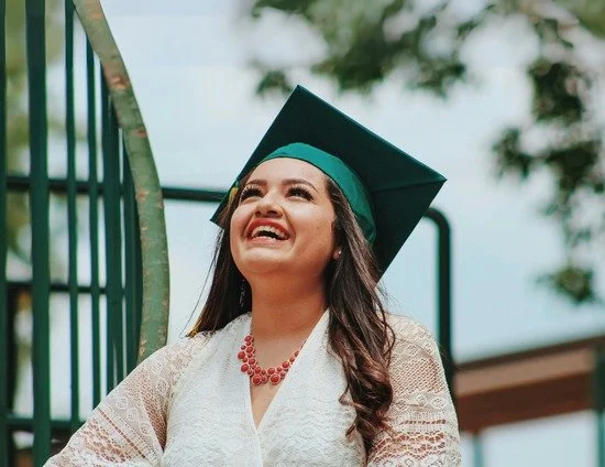 A woman in a graduation cap and gown smiling outdoors.