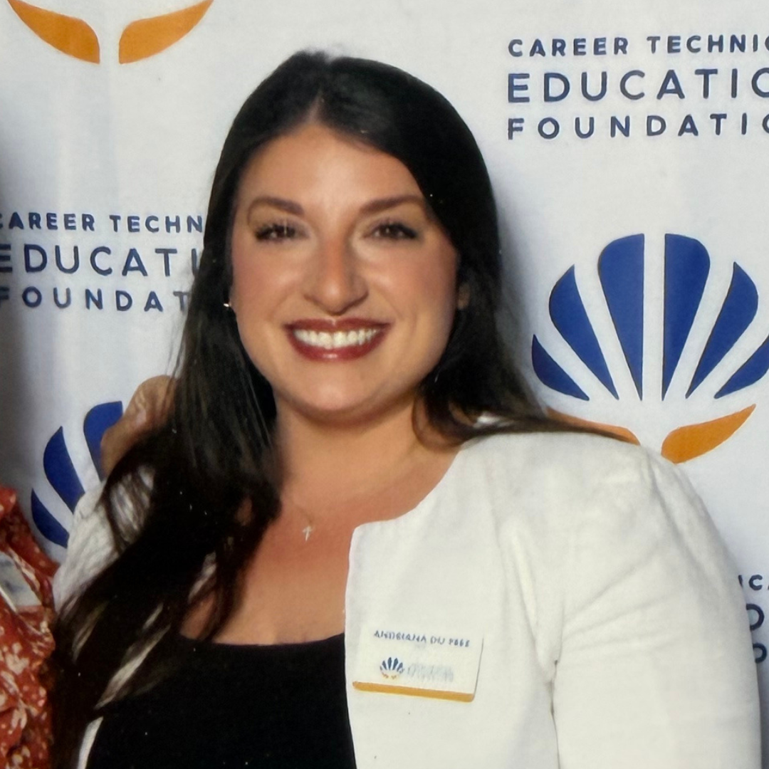 Smiling woman with dark hair wearing a white blazer and black top in front of a backdrop with logos and text reading 'Career Technical Education Foundation'.