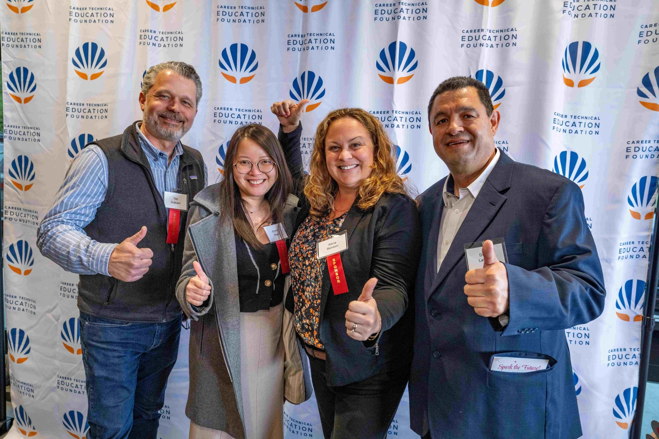 Group of five people posing in front of a backdrop with the logo and name of the Career Technical Education Foundation, smiling and giving thumbs-up gestures.