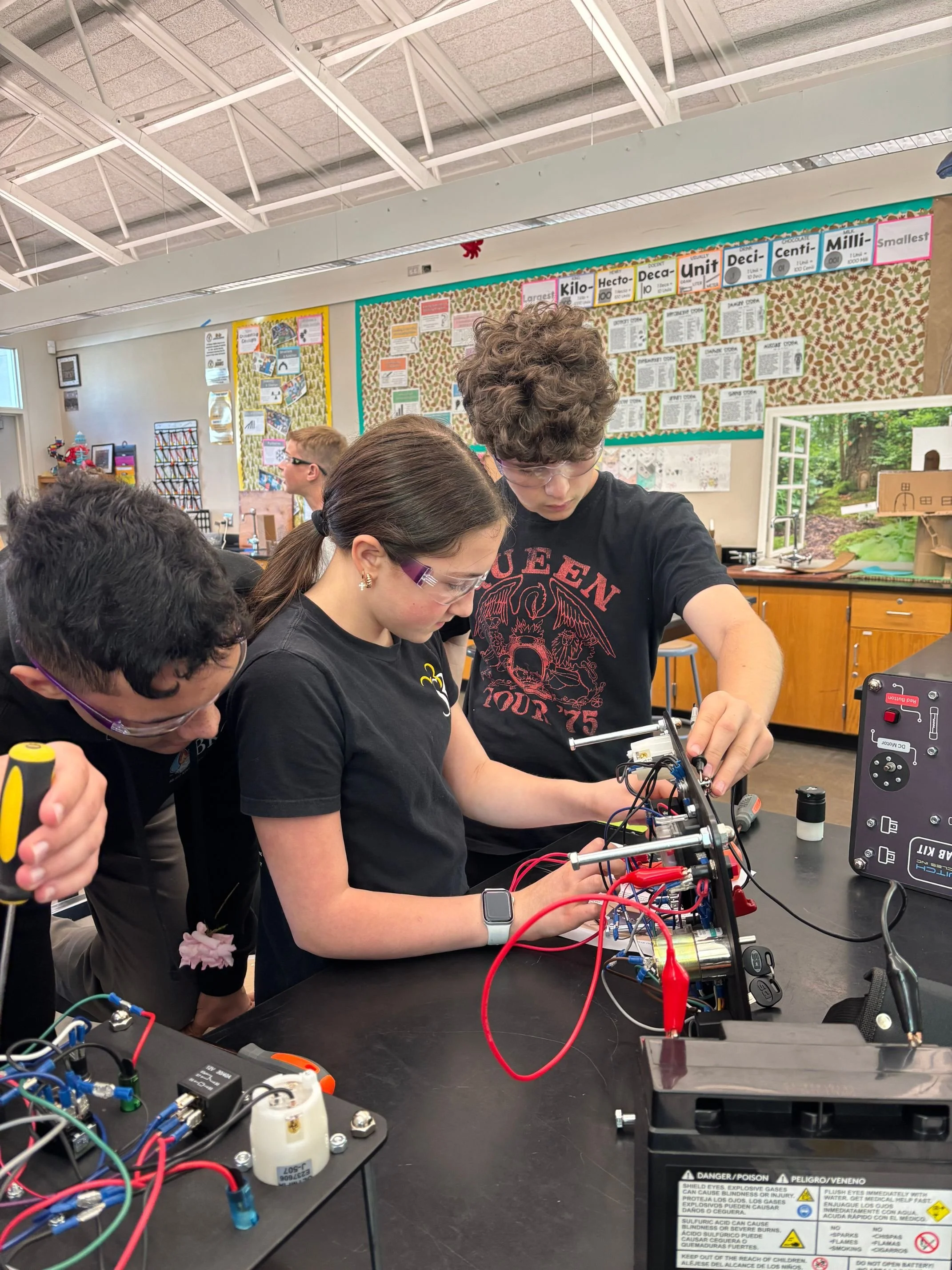 Group of students working on a science project involving electrical wiring and circuit components in a classroom.