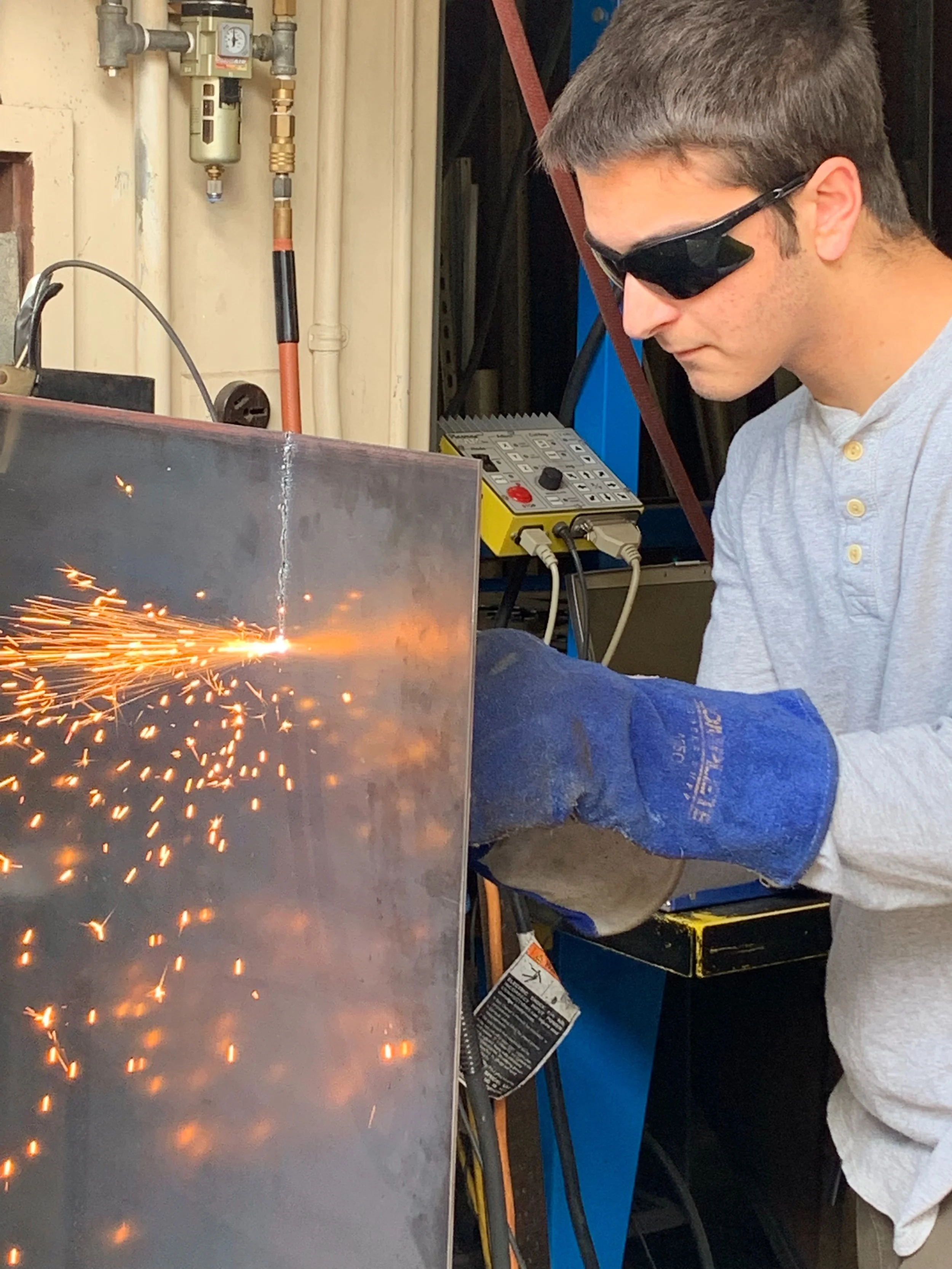 A person welding metal, wearing protective goggles, with sparks flying.
