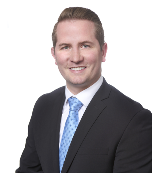 Portrait of a smiling man in a black suit, white shirt, and light blue tie against a plain white background.