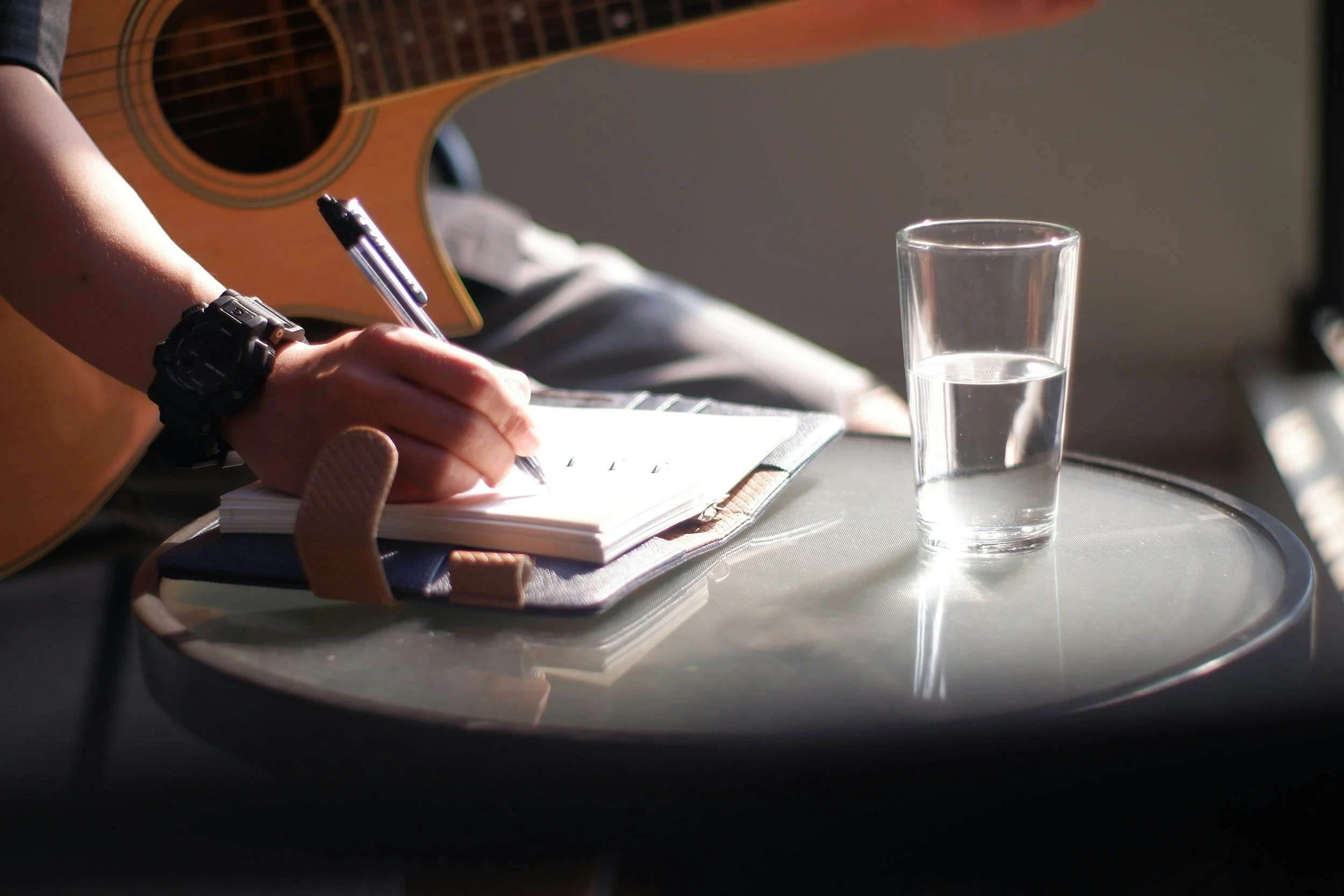 Image of someone writing songs with an acoustic guitar. Representing songwriting and authorship, and educational presentations.