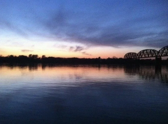 Blue-hour landscape featuring a calm Ohio River, colorful sunset reflections, and a railway bridge in the distance, photographed by Rob Smith
