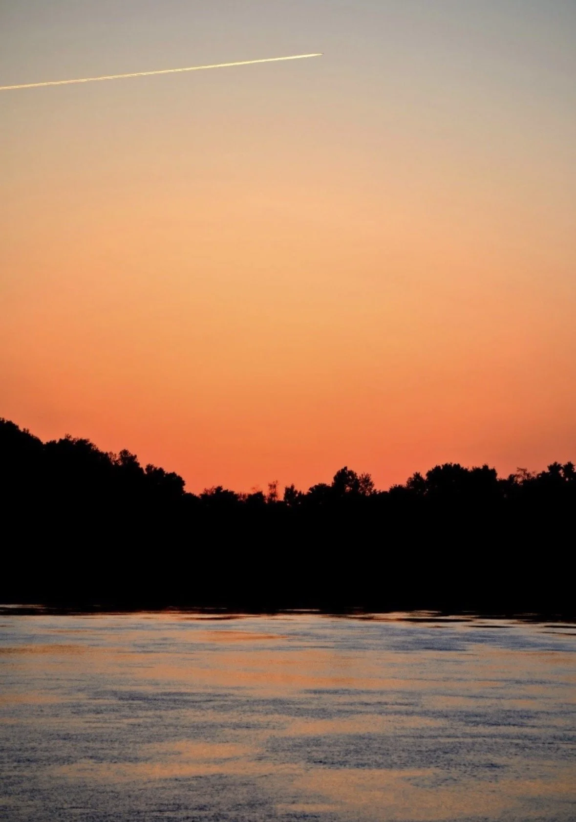 Golden sunset over a calm river with silhouetted trees reflected on the water, photographed by Rob Smith.