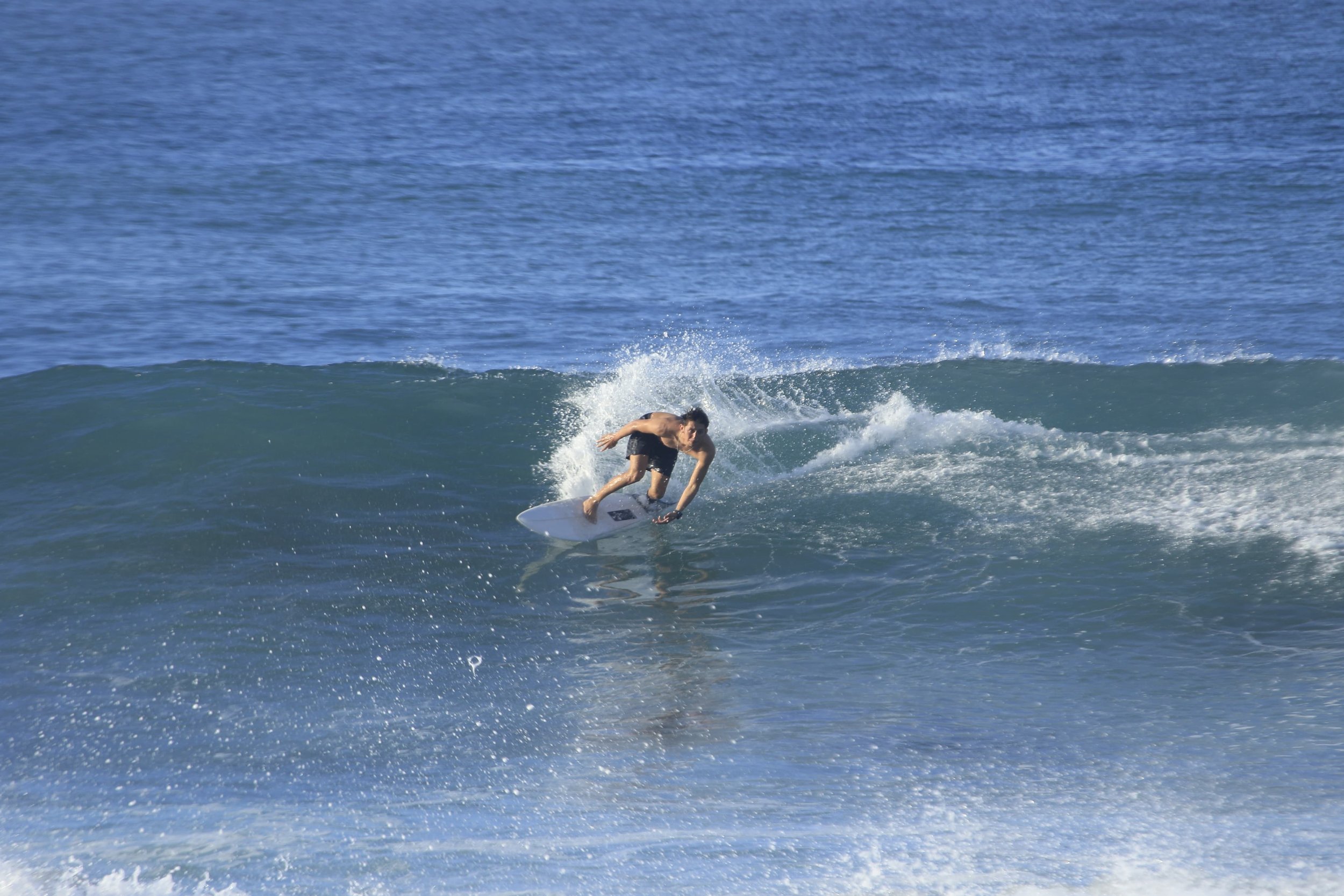 Surfer riding a wave in the ocean, leaning forward on a white surfboard.
