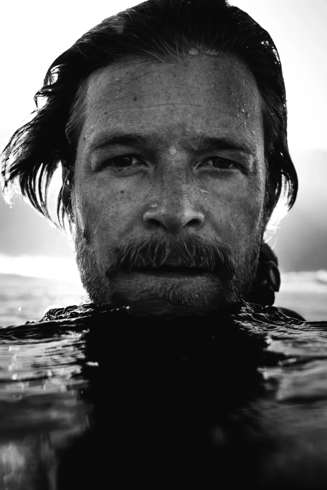 Schwarz-Weiß-Foto eines Mannes mit nassem Haar und Bart, der im Wasser bis zum Kinn steht.