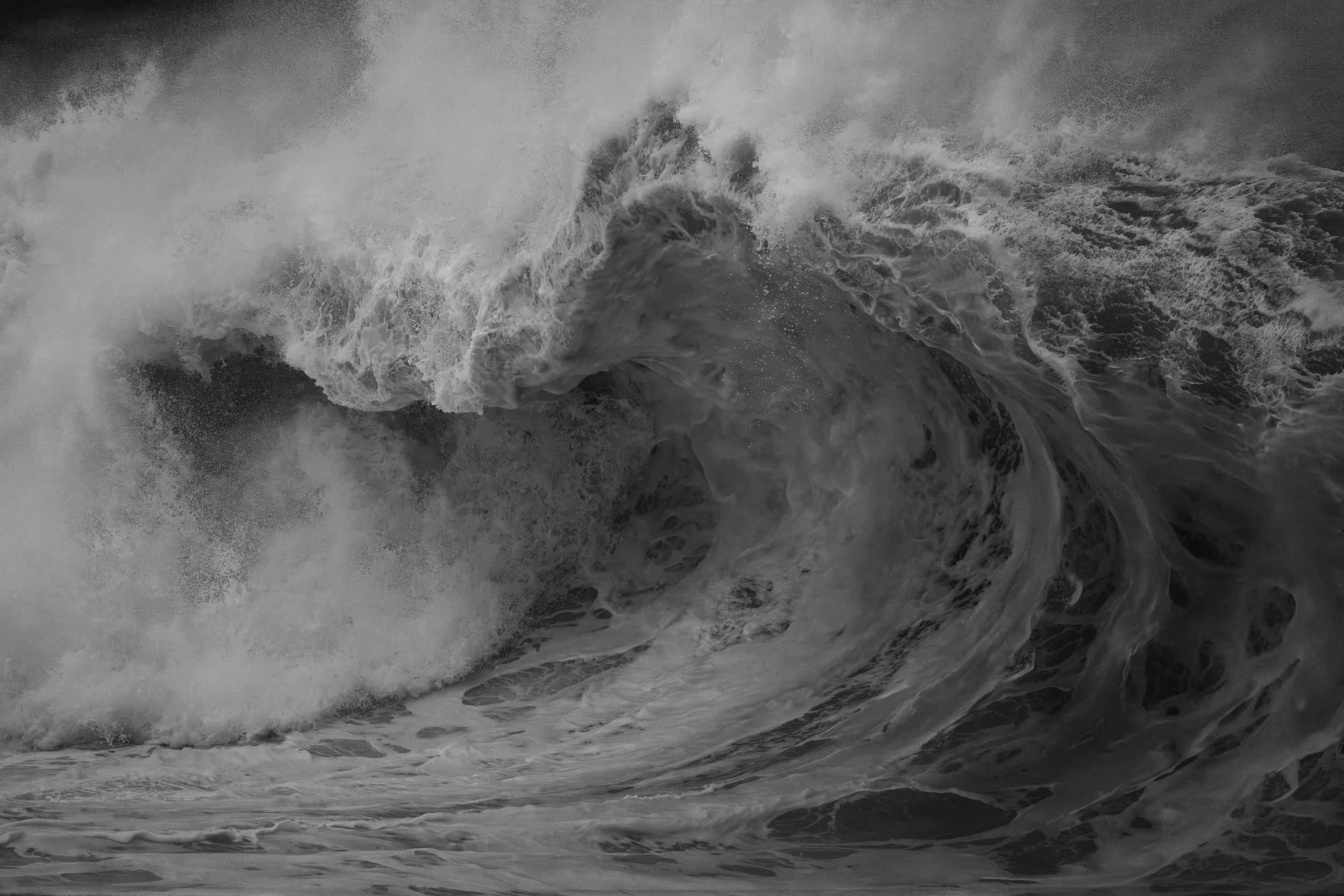 Das Bild zeigt eine große Welle im Meer, die aufgewühlt ist mit Schaum und Wasser, in Graustufen.