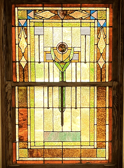 A stained glass window in The Bradshaw in Eudora, Kansas with a geometric design of symmetrical patterns in yellow, green, blue, and brown.