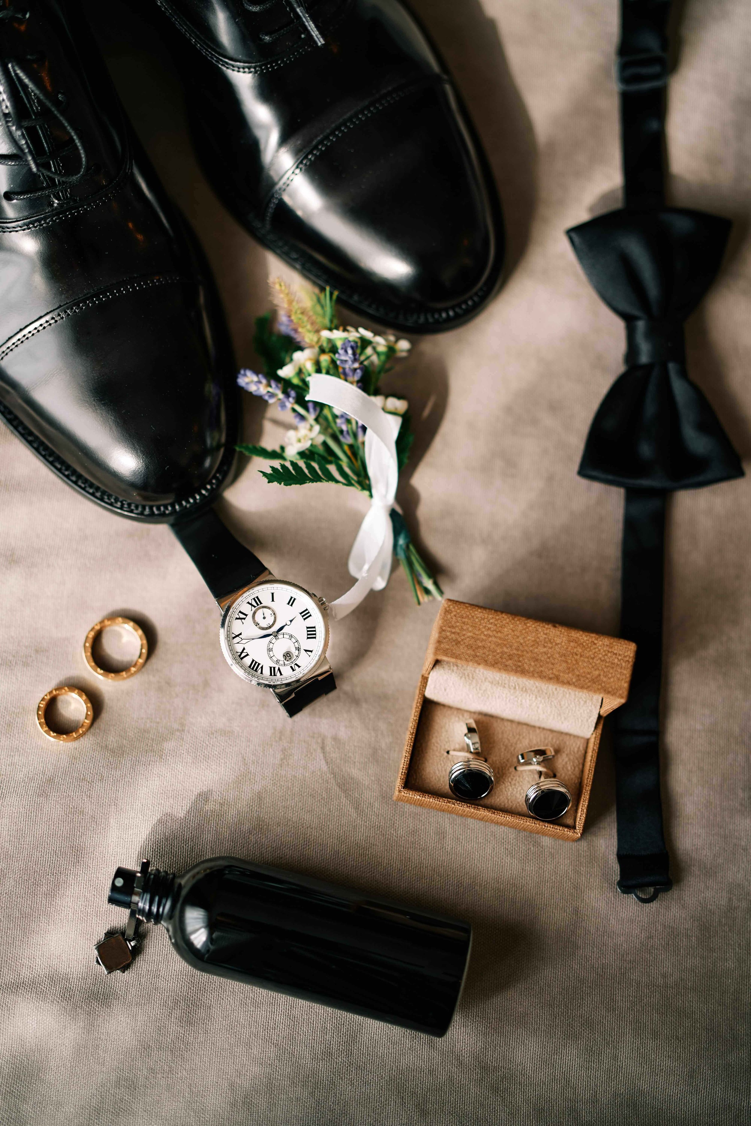 Shoes and accessories for a groom laid out on white cloth.