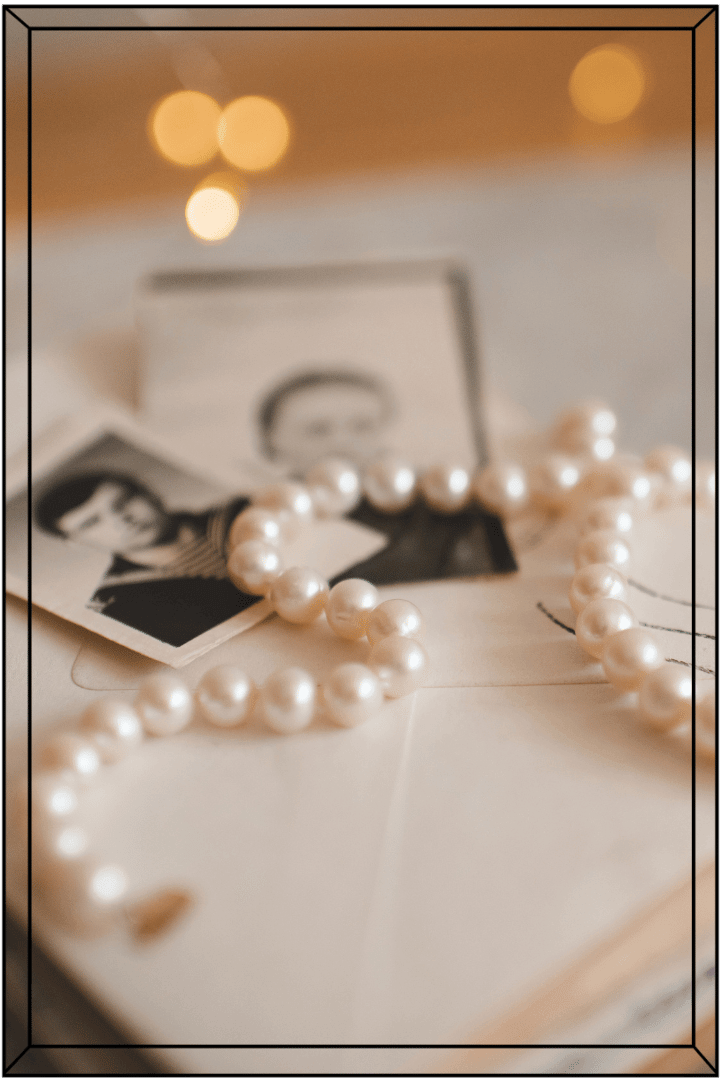 A pearl necklace, vintage black-and-white photographs, and a black-and-white portrait of a woman arranged on an envelope or letter.
