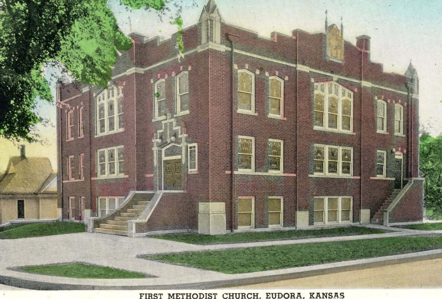 Postcard of the First Methodist Church in Eudora, Kansas, a red brick building with multiple windows and staircases on either side, surrounded by trees and grass.