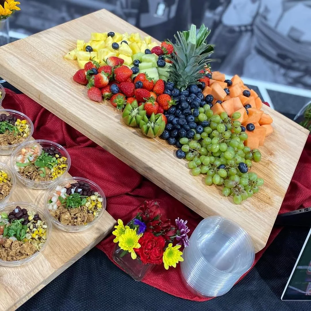 Assorted sliced fruits including pineapple, honeydew, cantaloupe, green and purple grapes, strawberries, blueberries, and a pineapple centerpiece on a wooden serving board.