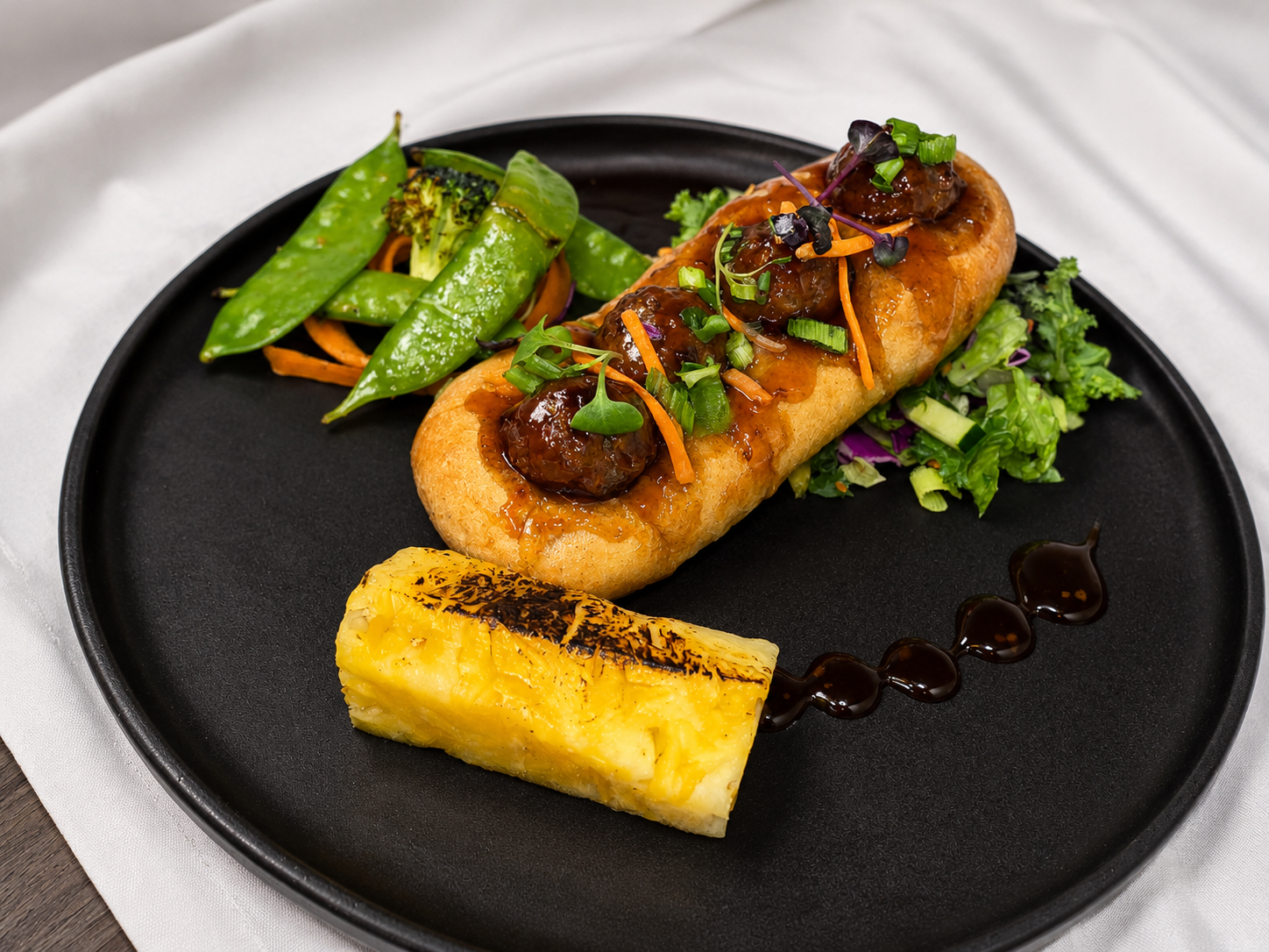 A plate with a stuffed pastry topped with sauce and garnished with green onions, served with grilled vegetables, a small salad, and a slice of grilled pineapple with a drizzle of sauce.