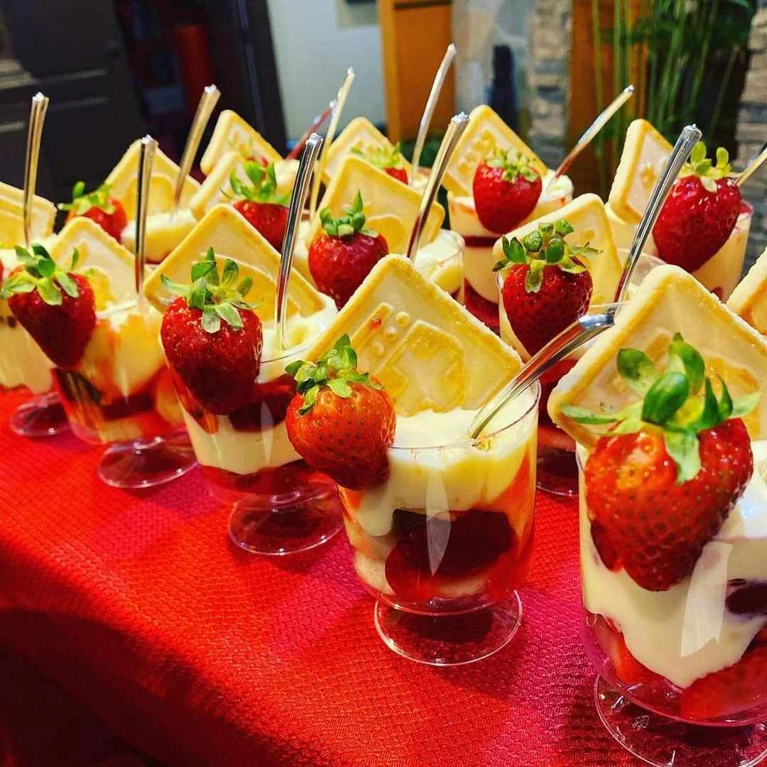 Individual strawberry and vanilla parfaits with chocolate layer at the bottom, garnished with fresh strawberries and a square cookie, served on a red tablecloth.