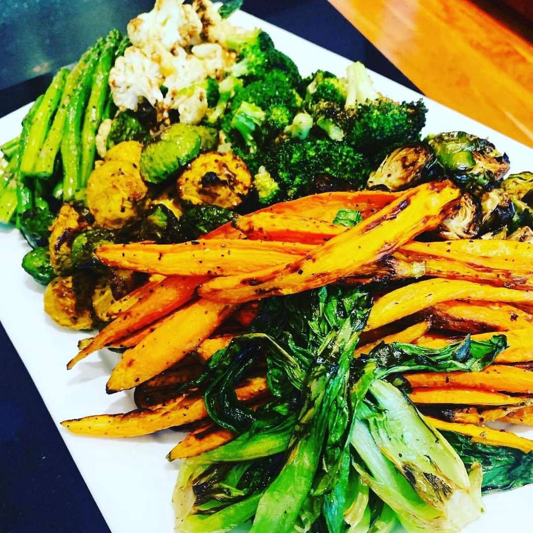 A plate of grilled mixed vegetables including carrots, bok choy, broccoli, cauliflower, asparagus, and Brussels sprouts.