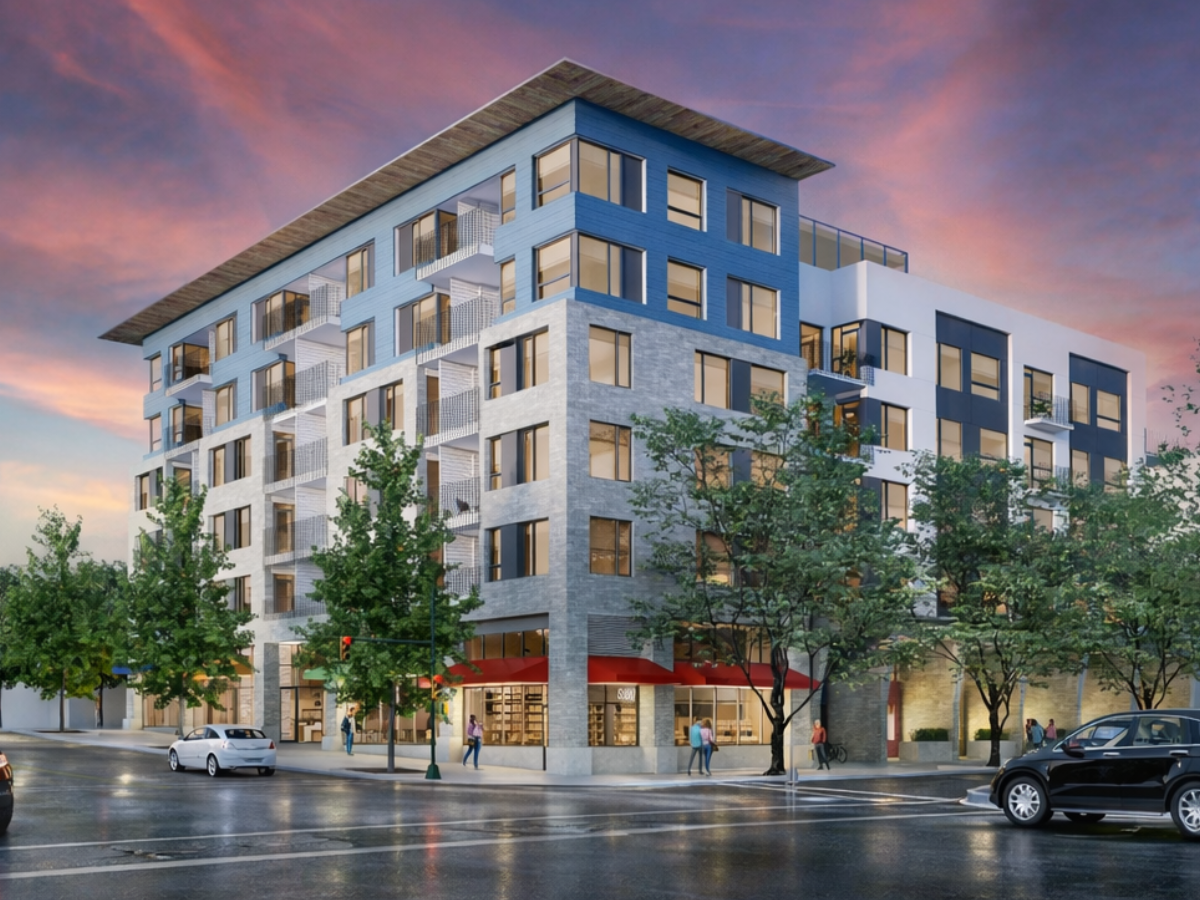 A modern multi-story apartment building with retail shops on the ground floor, located on a city street with cars, pedestrians, and trees during sunset.