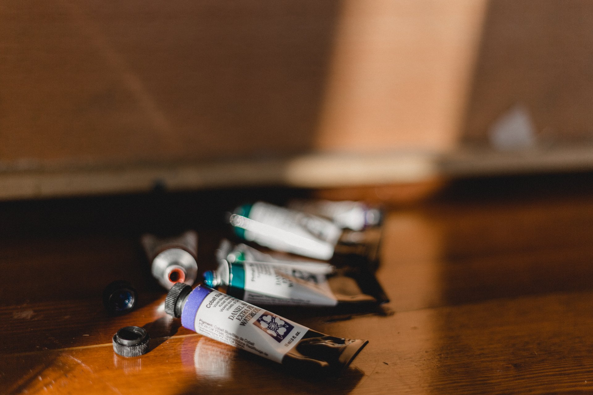 Paint tubes and caps scattered on a wooden surface, some open, with a blurred background.