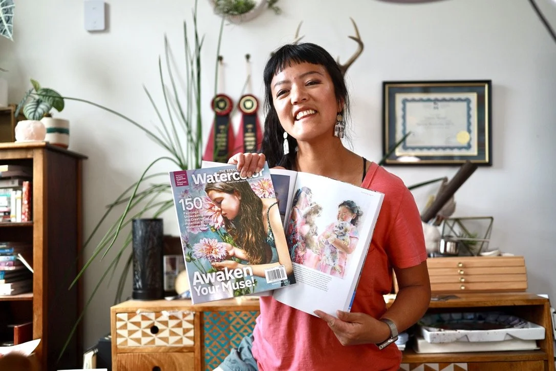 Woman smiling and holding an open magazine with a cover titled 'Watercolor' and a woman holding flowers.