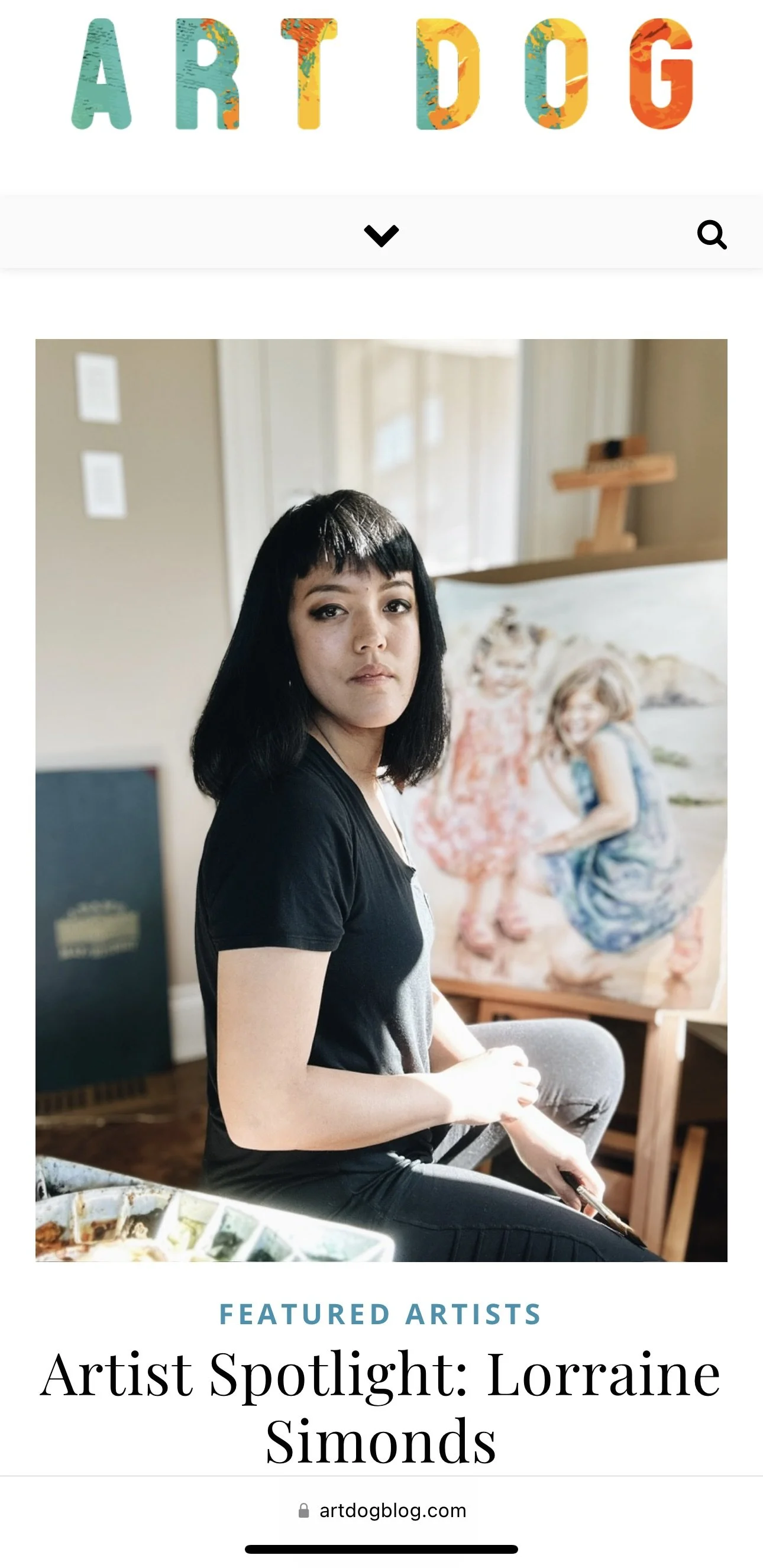A woman with black hair and bangs sitting indoors in front of a colorful painting of two young girls.
