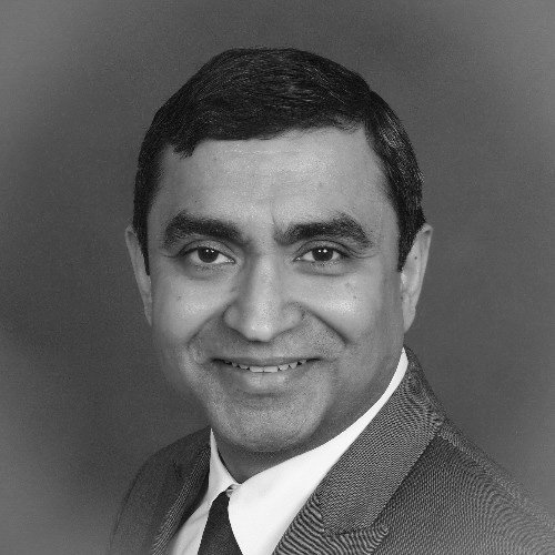 Black and white headshot of a man with short, dark hair, wearing a suit jacket, white shirt, and tie, smiling at the camera.